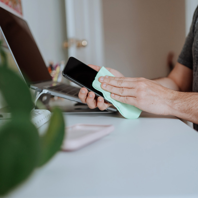 Hand wischt mit einem Mikrofasertuch über ein Smartphonedisplay