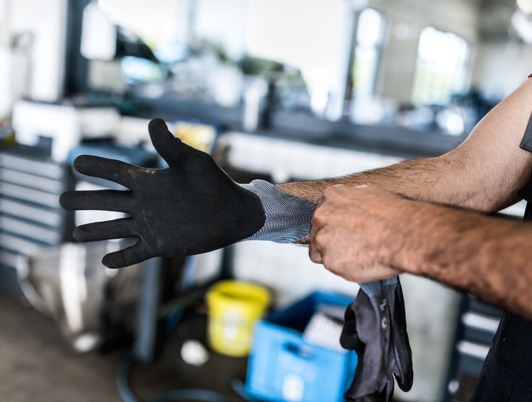 Mann in Werkstatt zieht sich einen schwarzen Handschuh an