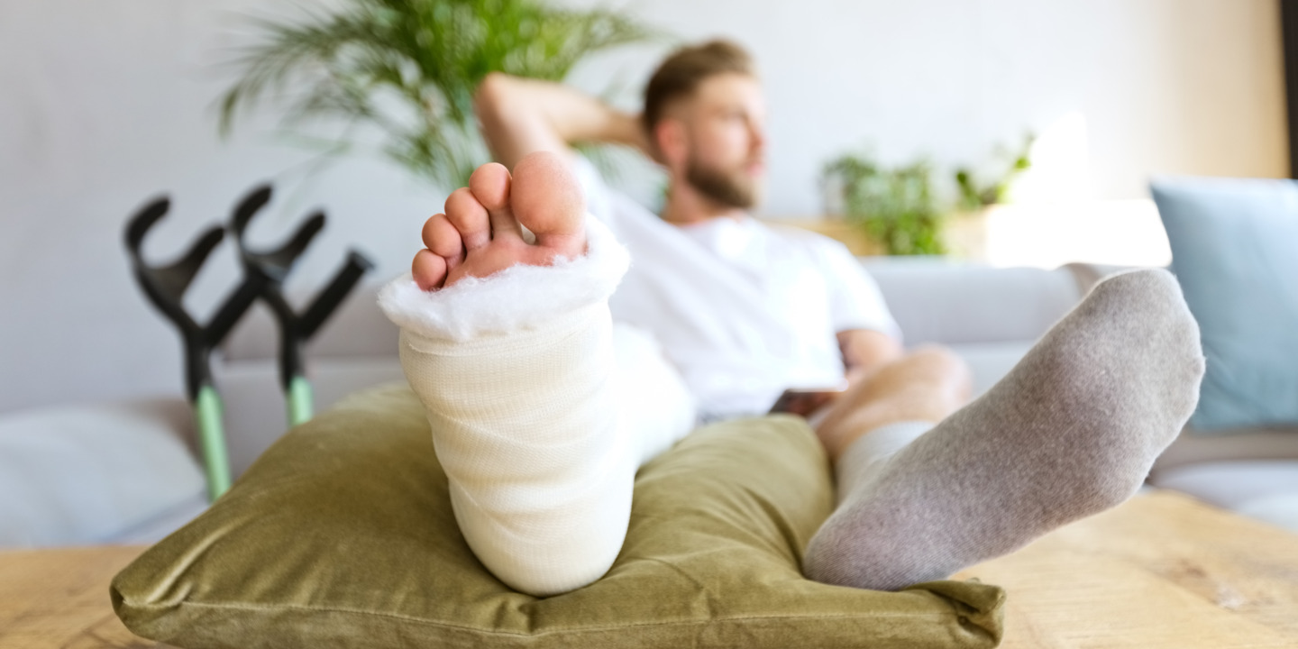 Junger Mann liegt mit einem Gips am Bein auf der Couch