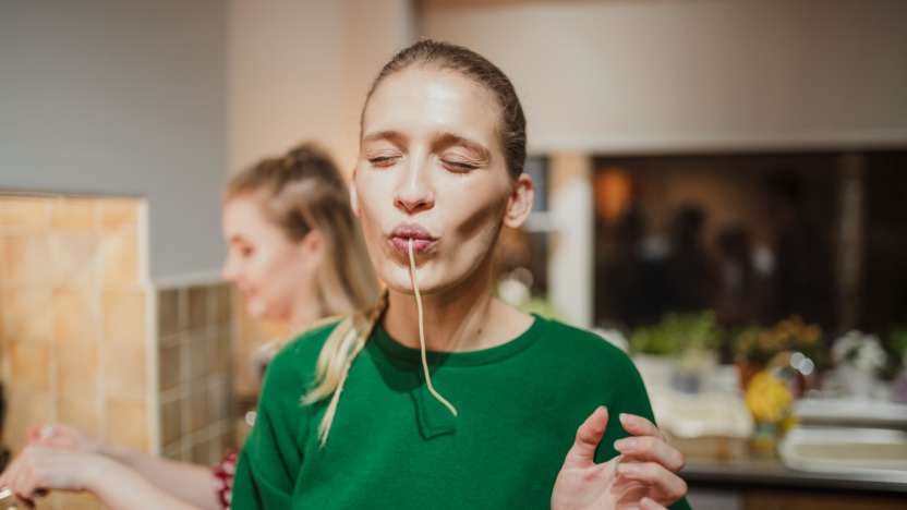 Frau steht in der Küche und genießt eine Spaghetti.
