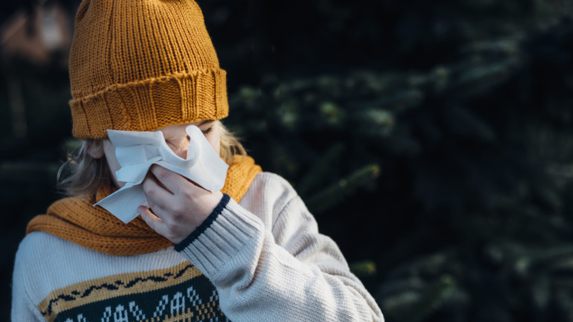 Kind in Winterkleidung putzt sich mit einem Taschentuch die Nase