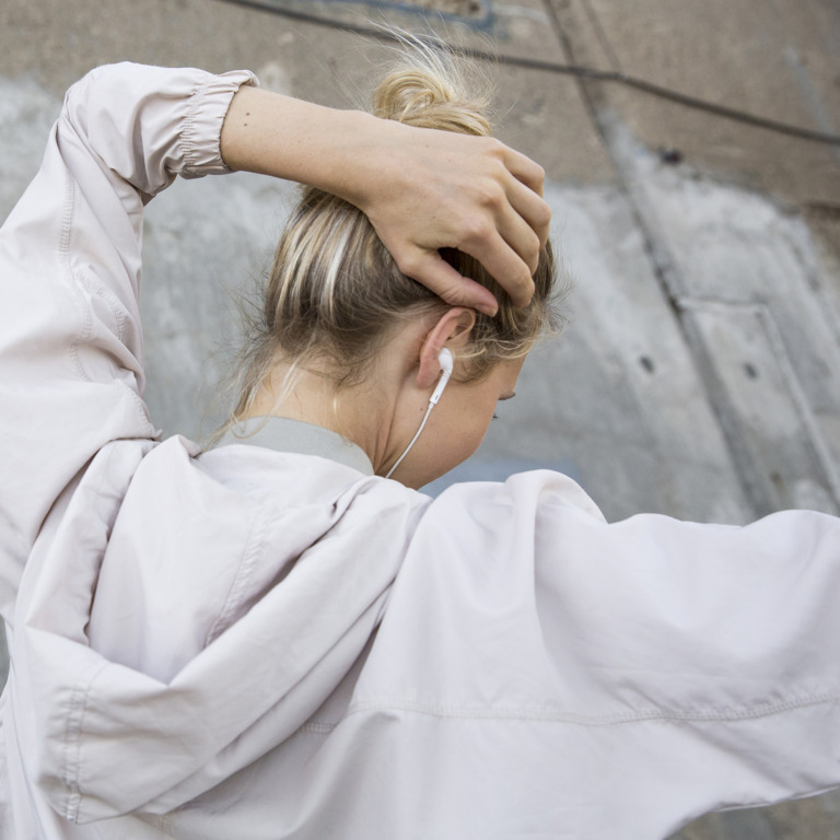 junge Frau mit In-Ear-Kopfhörern fasst sich gestresst an den Hinterkopf