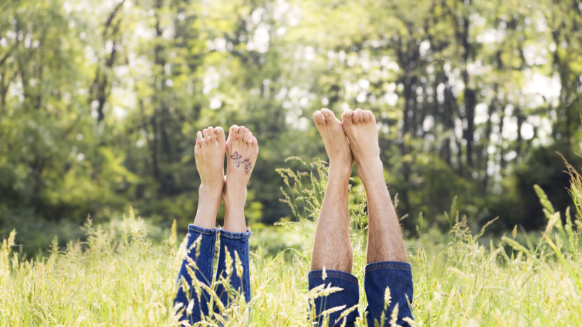 Mann und Frau liegen auf dem Rücken in einer Wiese und recken ihre nackten Füße in die Luft