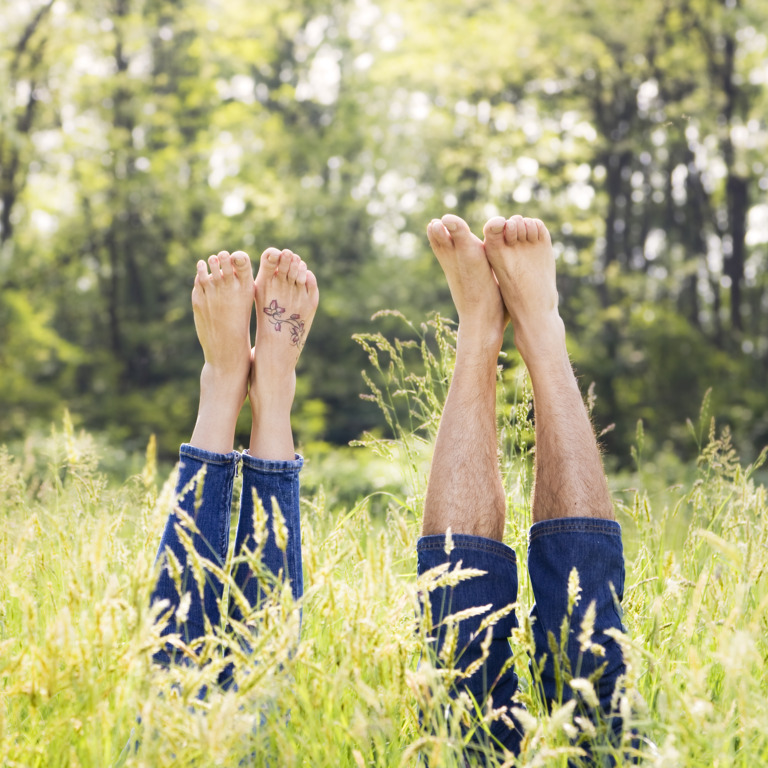 Mann und Frau liegen mit dem Rücken auf einer Wiese und strecken ihre nackten Füße in die Luft