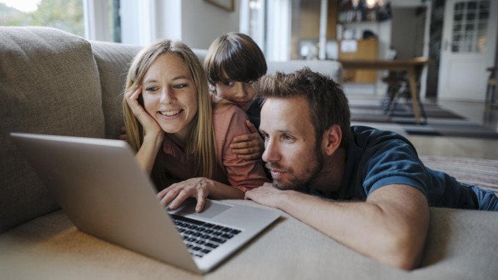 Dreiköpfige Familie liegt gemeinsam vor einen Laptop
