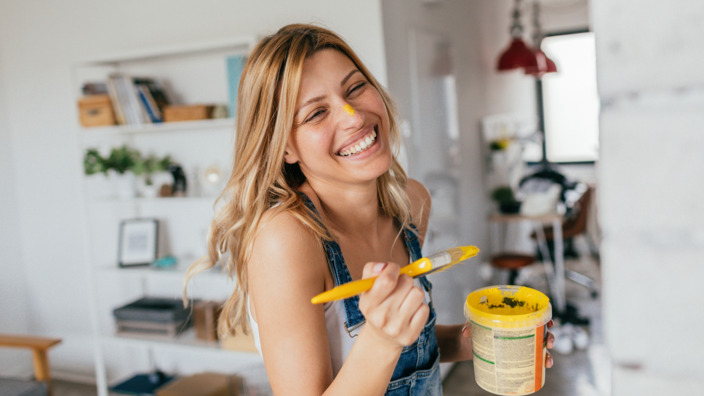junge Frau lackiert einen Schrank mit gelber Farbe