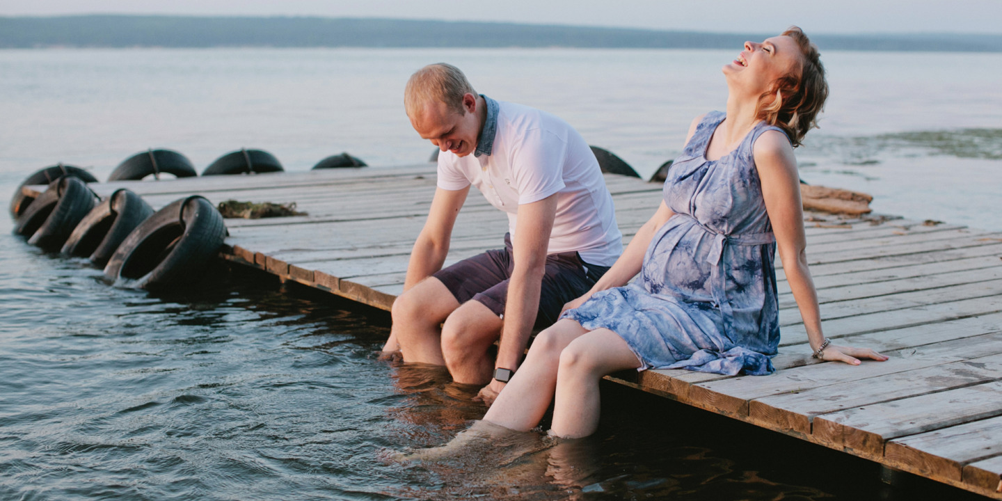 werdende Eltern sitzen auf einem Steg am See