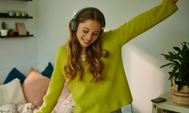 Junge Frau mit Kopfhörern tanz in ihrem Zimmer
