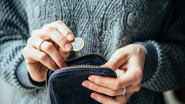 Hand hält eine Ein-Euro-Münze und steckt sie in ein Portemonnaie
