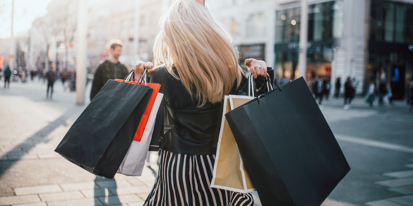 Frau geht mit vollen Shopping-Tüten durch eine Einkaufsmeile