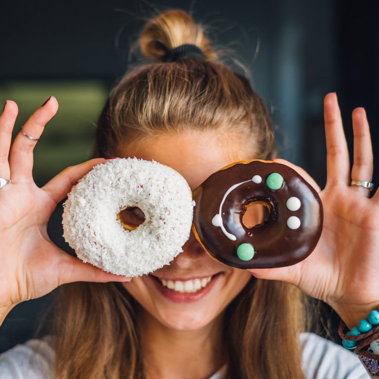 junge Frau schaut lachend durch zwei bunt dekorierte Donuts
