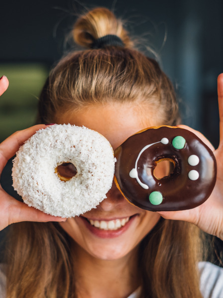 junge Frau schaut lachend durch zwei bunt dekorierte Donuts