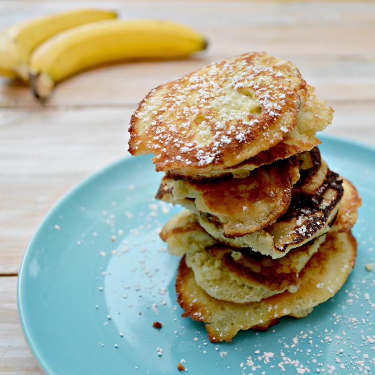 Ein Teller mit Bananen-Pancakes und Bananen im Hintergrund.