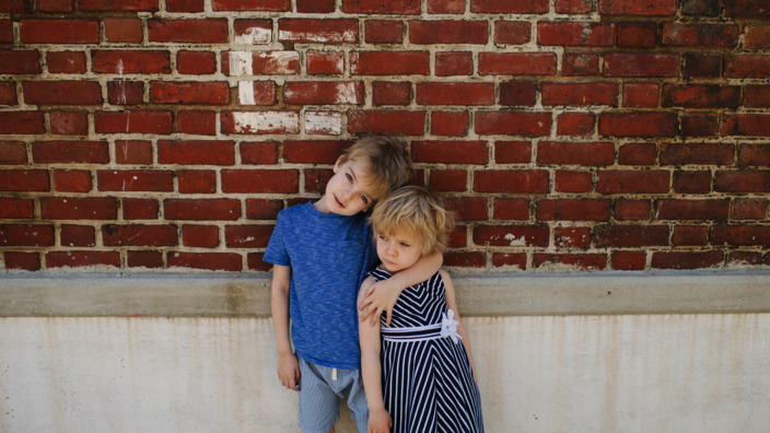 Bruder und Schwester stehen Arm in Arm vor einer Hauswand