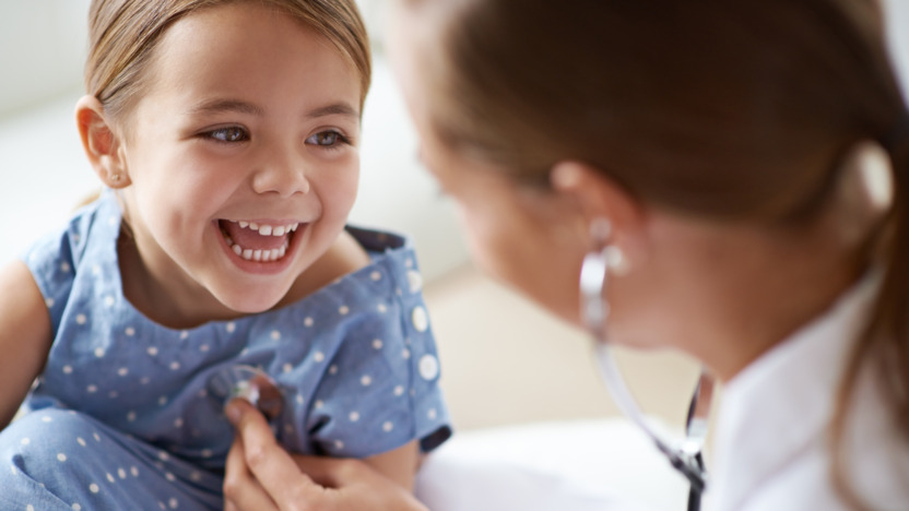 Kinderärztin hört ein lächelndes kleines Mädchen mit dem Stethoskop ab.