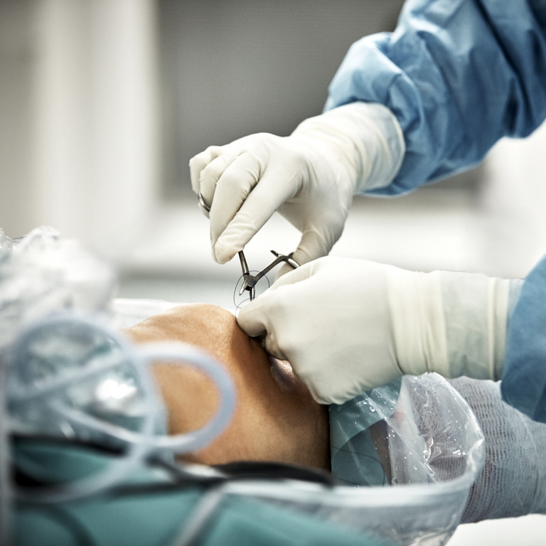 Arzt schneidet Fäden an einem operierten Knie ab