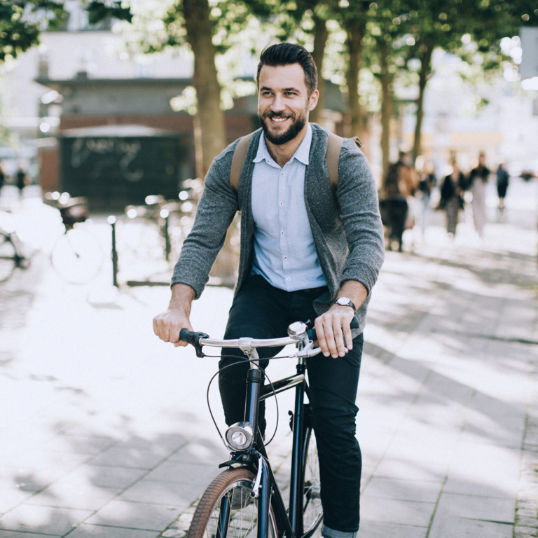 Der junge Man mit Bart fährt im Sommer mit dem Fahrrad zur Arbeit.
