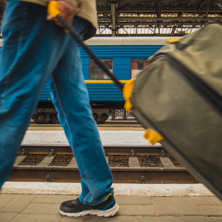 Person mit Koffer am Bahnhof vor Zug in ukrainischen Farben