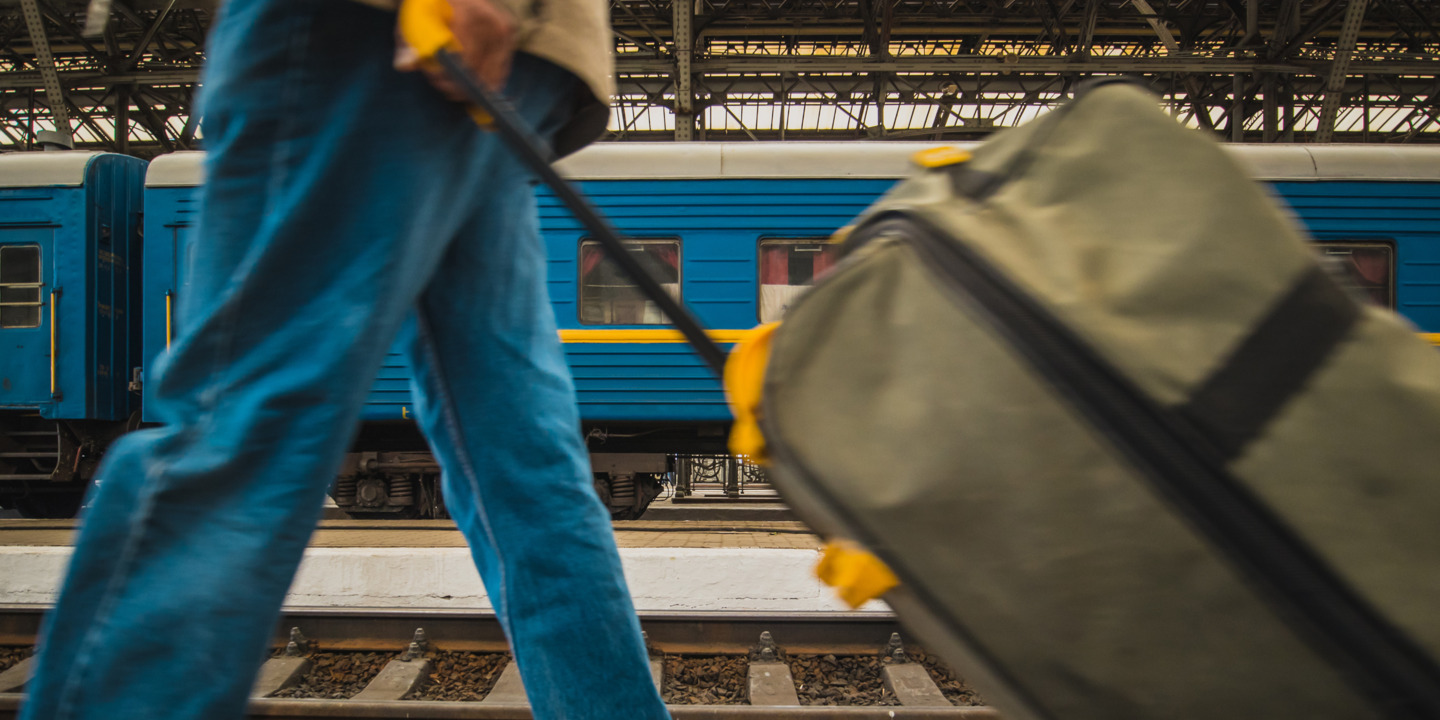 Person mit Koffer am Bahnhof vor Zug in ukrainischen Farben