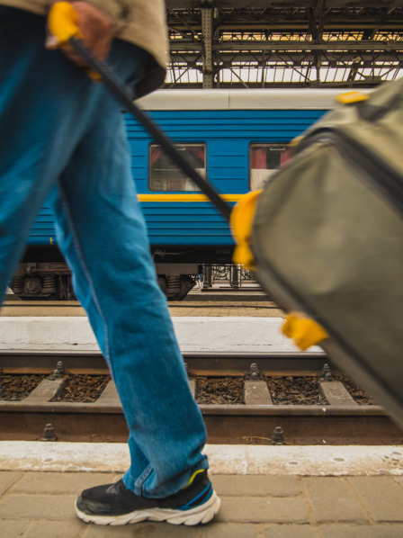 Person mit Koffer am Bahnhof vor Zug in ukrainischen Farben