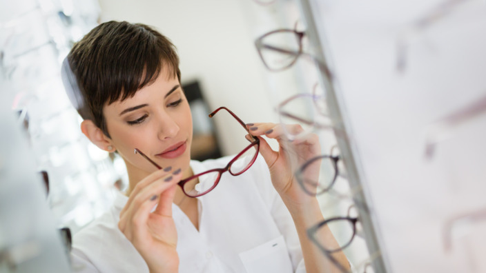 Junge Frau probiert Brille vor einem Spiegel im Brillengeschäft