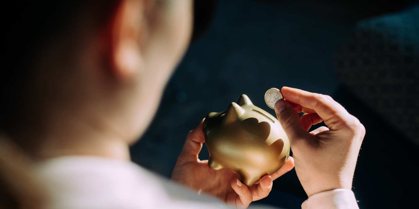 Person steckt 1-Euro-Münze in Sparschwein