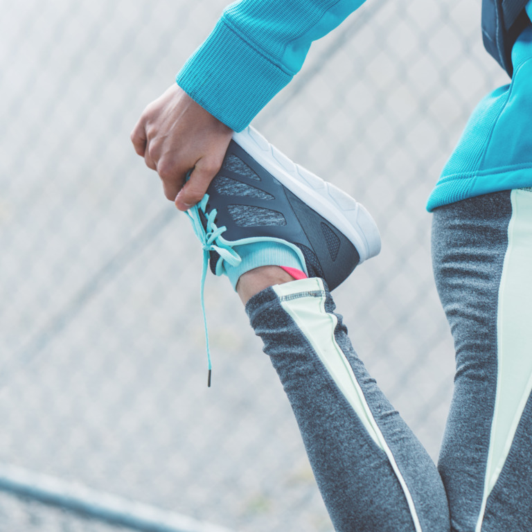 Person in Sportkleidung dehnt das rechte Bein.