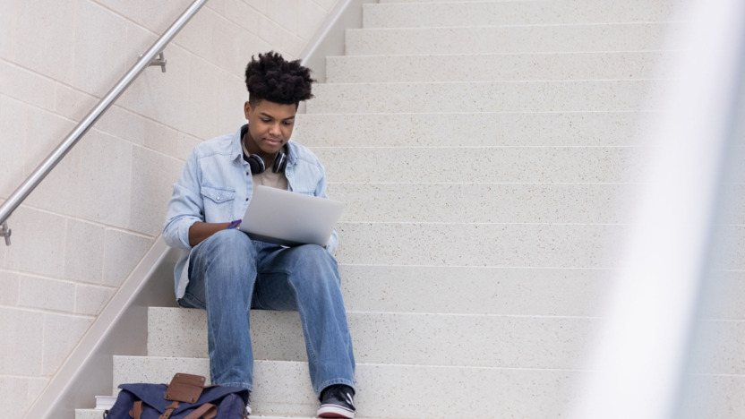 Junge Person sitzt mit dem Laptop auf dem Schoß auf einer Treppe. 