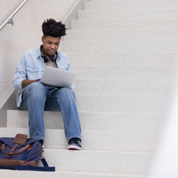 Junger Mann sitzt auf Treppe und schreibt eine Bewerbung.