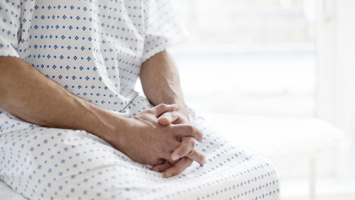 Patient sitzt in OP-Kittel auf dem Rand eines Krankenhausbettes
