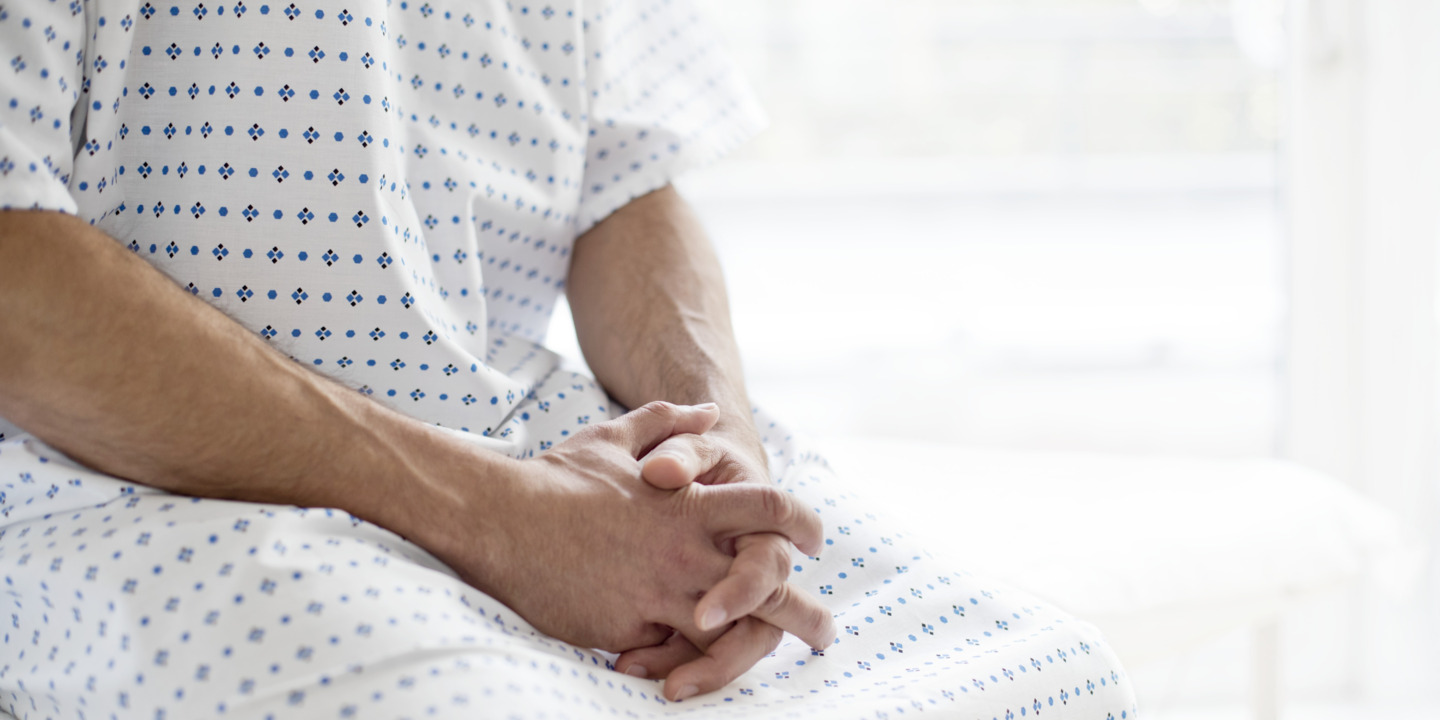 Patient sitzt im OP-Kittel auf dem Rand eines Krankenhausbettes