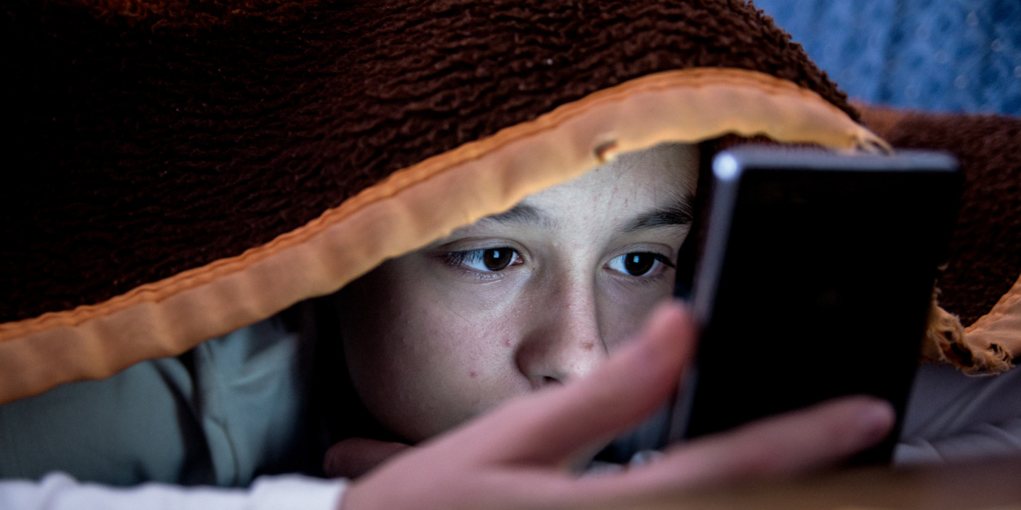 Kind schaut, versteckt unter eine Decke, auf das Display eines Smartphones