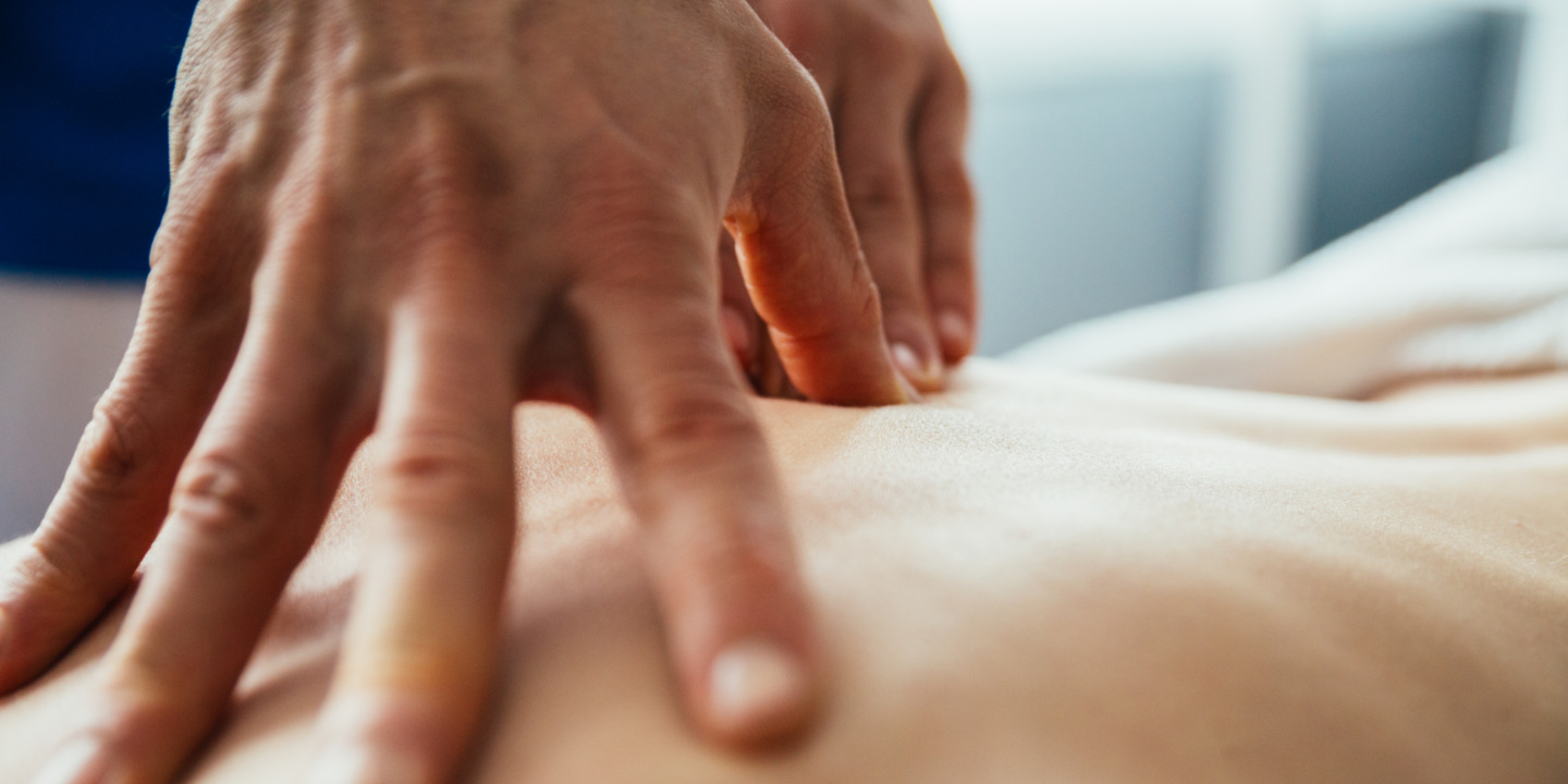 Hände eines Therapeuten behandeln Rücken eines Patienten.