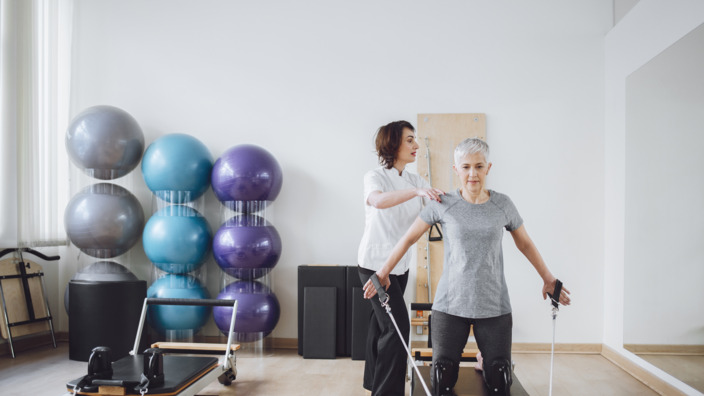 ältere Frau absolviert Pilatesübungen mit einer Trainerin