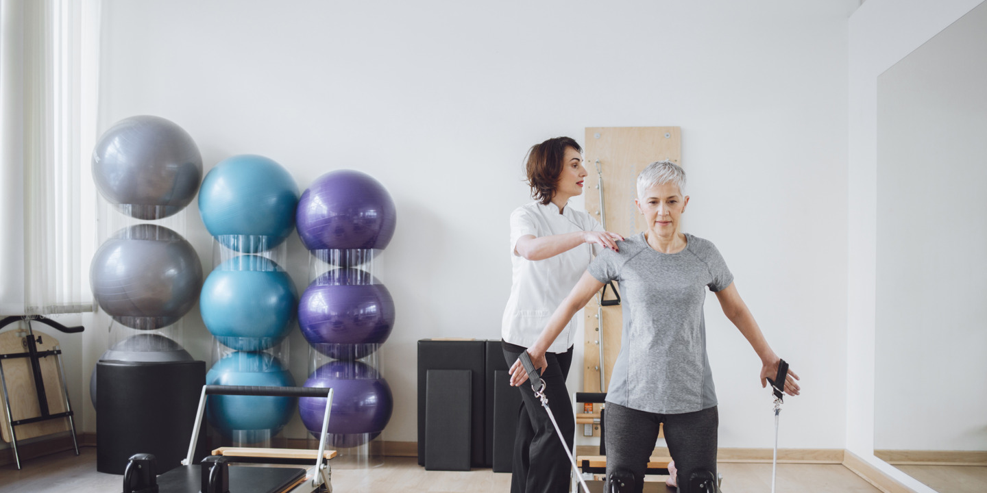 ältere Frau absolviert Pilatesübungen mit einer Trainerin