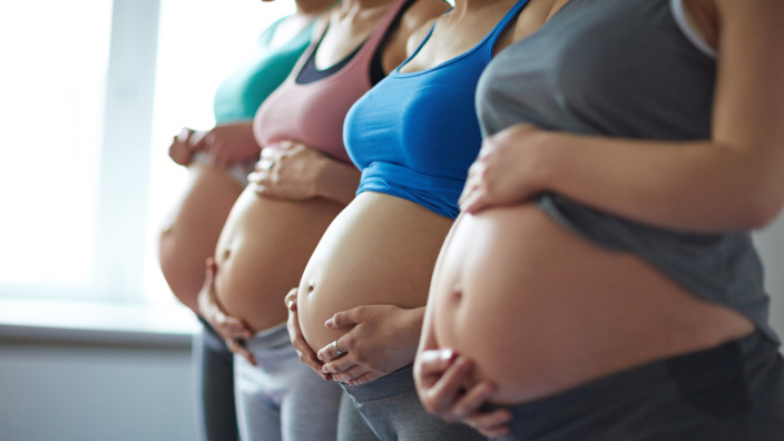 Vier Schwangere stehen nebeneinander und zeigen ihren Bauch