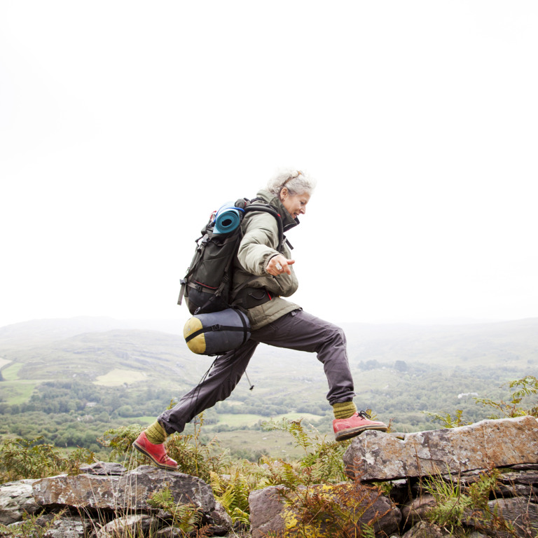 Frau mit Wanderausrüstung balanciert auf einer Steinmauer.