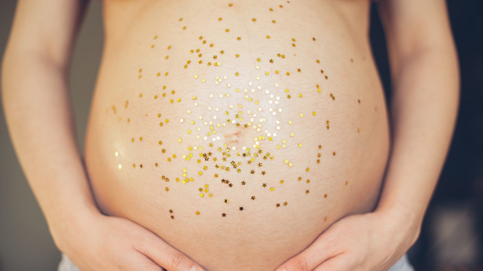 mit goldenem Konfetti dekorierter nackter Bauch einer Schwangeren