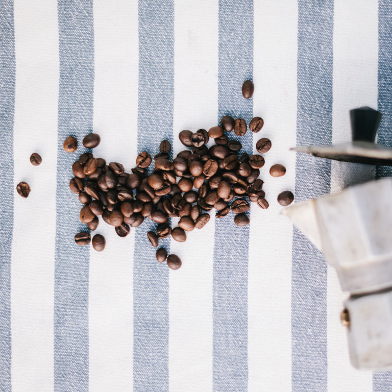 Espressokanne und Kaffeebohnen auf einer gestreiften Tischdecke.