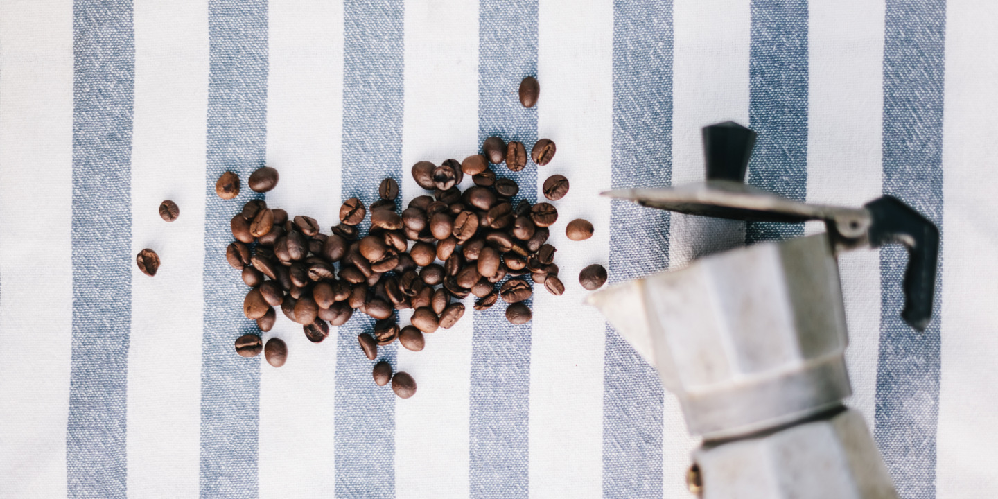 Espressokanne und Kaffeebohnen auf einer gestreiften Tischdecke