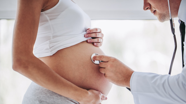 Frauenarzt horcht den Bauch einer Schwangeren mit dem Stethoskop ab