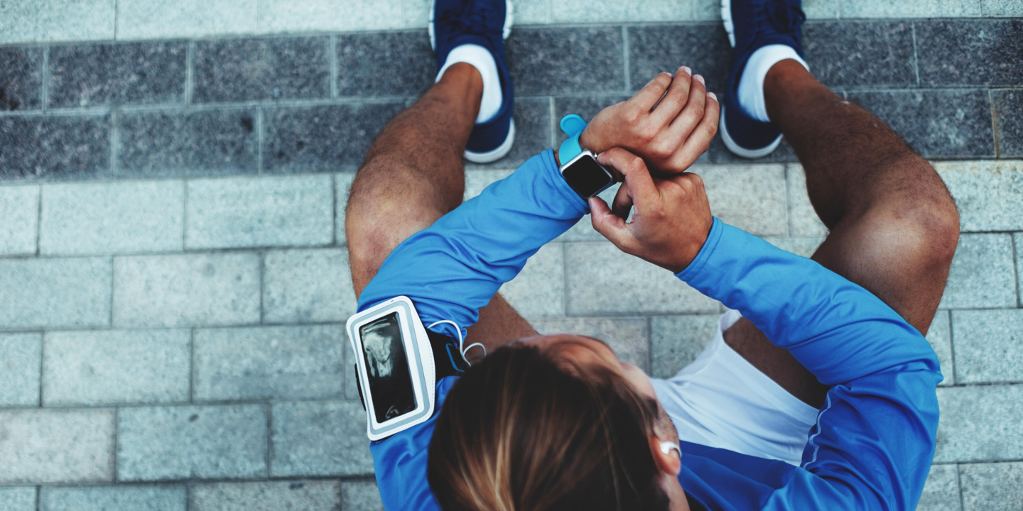 Ein in Sportsachen gekleideter, junger Mann, der auf seine Smartwatch guckt.