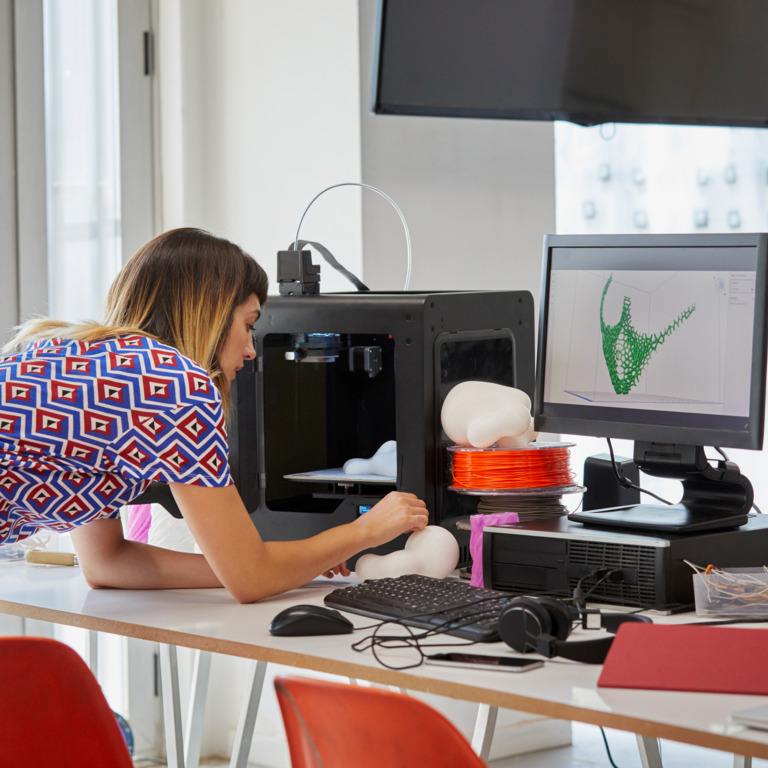 Frau baut am Schreibtisch ein Modell nach, dass sie am Computer entworfen hat.