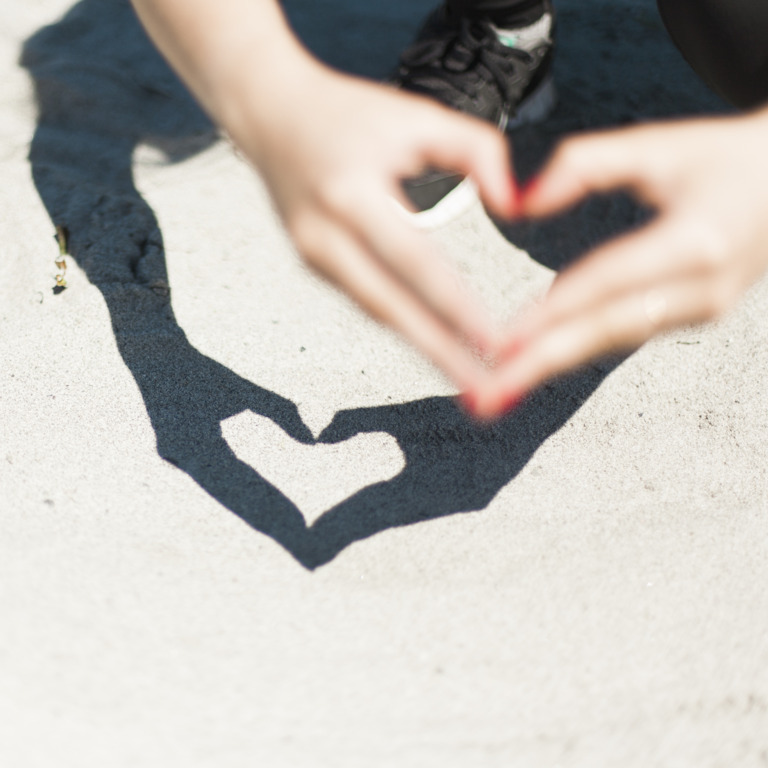 Hände einer Person bilden ein Herz und werfen einen Schatten in Herzform auf den Boden.