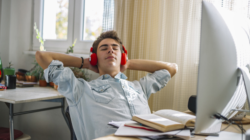 Junger Mann mit roten Kopfhörern sitzt am Schreibtisch und entspannt.