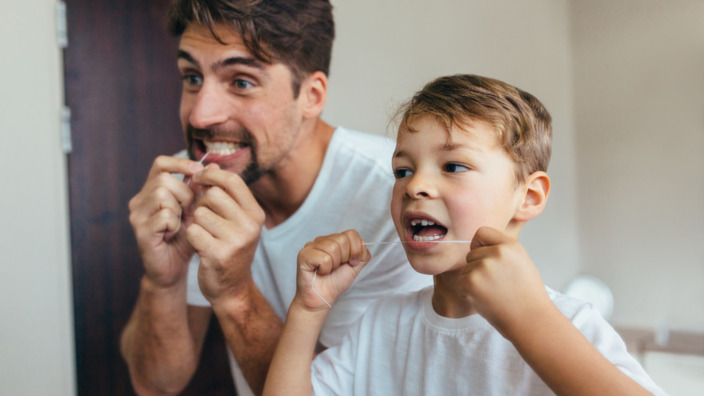 Vater und Sohn reinigen Zähne vor dem Spiegel mit Zahnseide