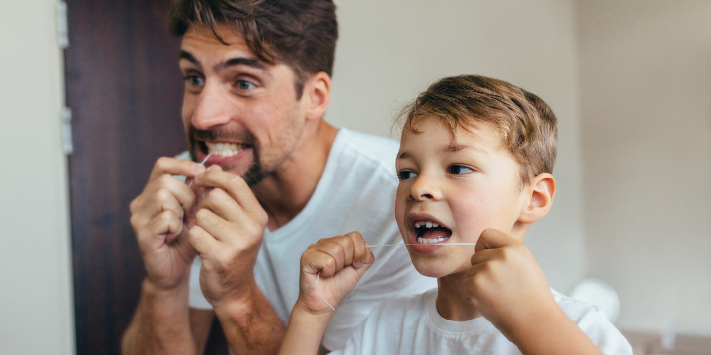 Vater und Sohn reinigen ihre Zähne mit Zahnseide und schützen sich so vor Parodontitis