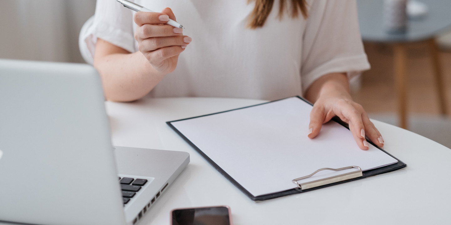 Junge Frau sitzt am Schreibtisch mit einem Labtop und einem Stift in der Hand