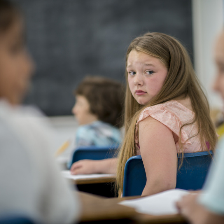 Schülerin die verängstigt ihre Schulkameraden in der Klasse anschaut.