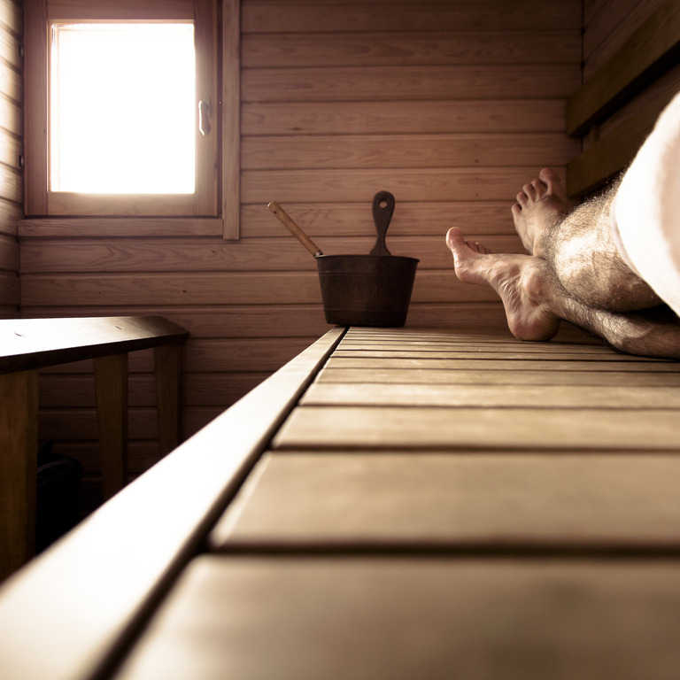 nackte Männerbeine liegen auf einer Holzliege in einer Sauna
